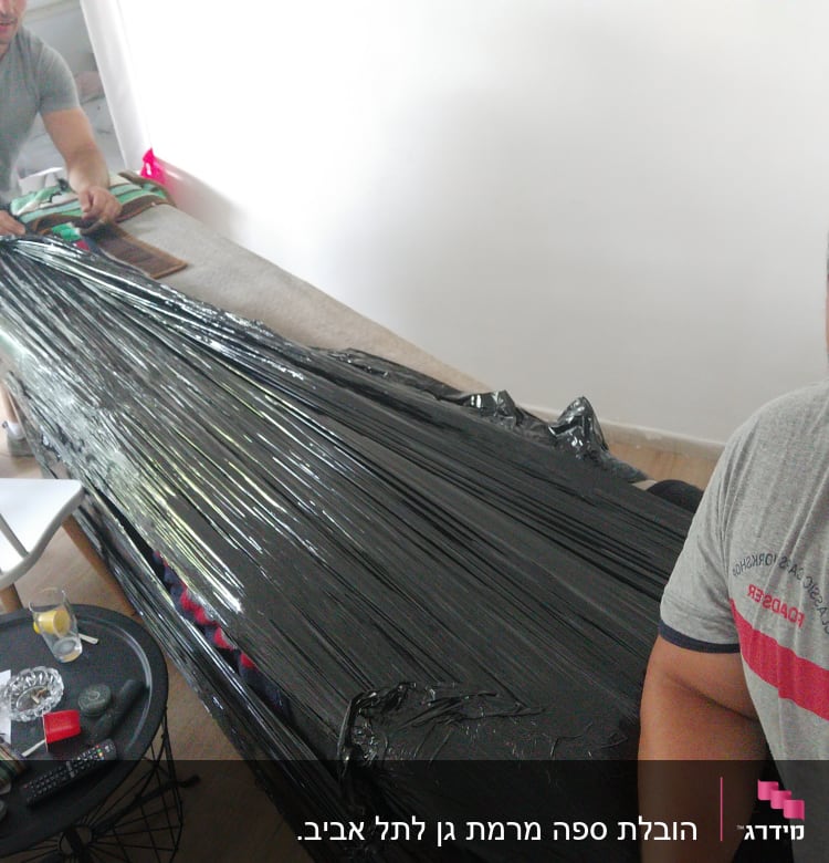 שני אנשים עוטפים רהיט בניילון שחור למעבר דירה